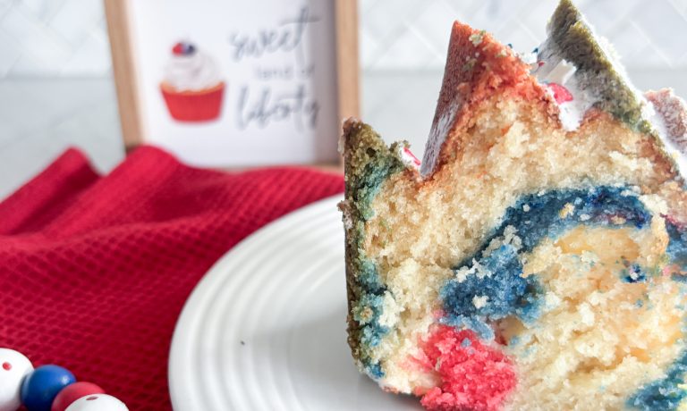 slice of bundt cake with red white and blue swirls on white plate, red napkin, red white and blue beads and sign that says sweet land of liberty