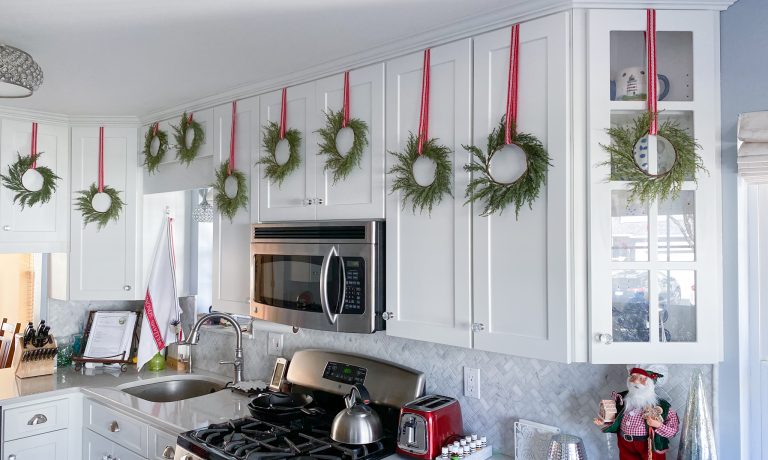 White shaker kitchen cabinets with green wreaths hung with red and white ribbons