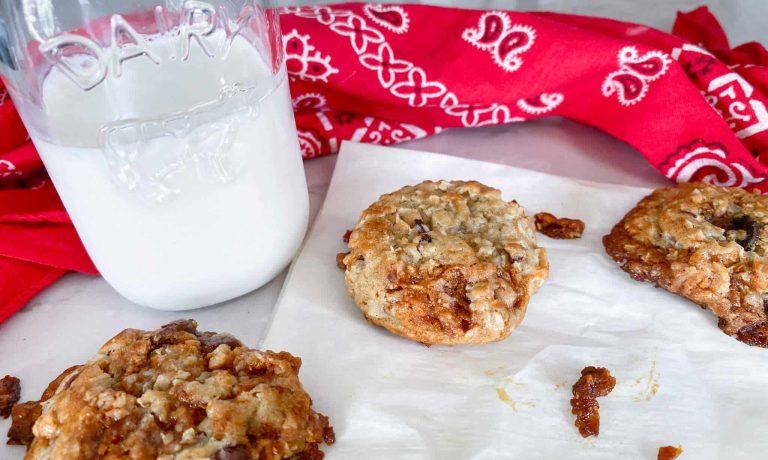 3 bacon chocolate chip cookies with glass of milk and red/white bandana on parchment